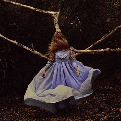 Photo of a woman in a lavender dress, and tree branches with human hands at their ends are grabbing her.