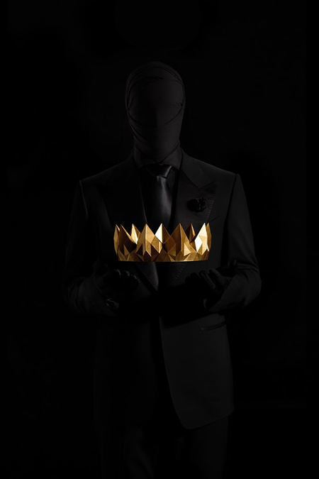 A person dressed all in black and masked is holding a golden crown