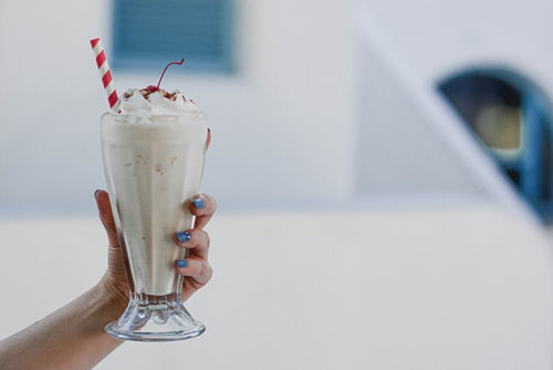Photo of a hand holding a milkshake in a tall glass, and a red and white striped straw sticks out of the top of the milkshake.