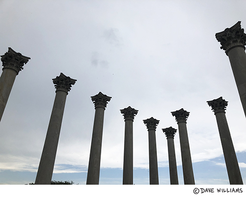 Photo of several columns arranged in a square with no building above them. A wide stretch of overcast cloud is above them instead.